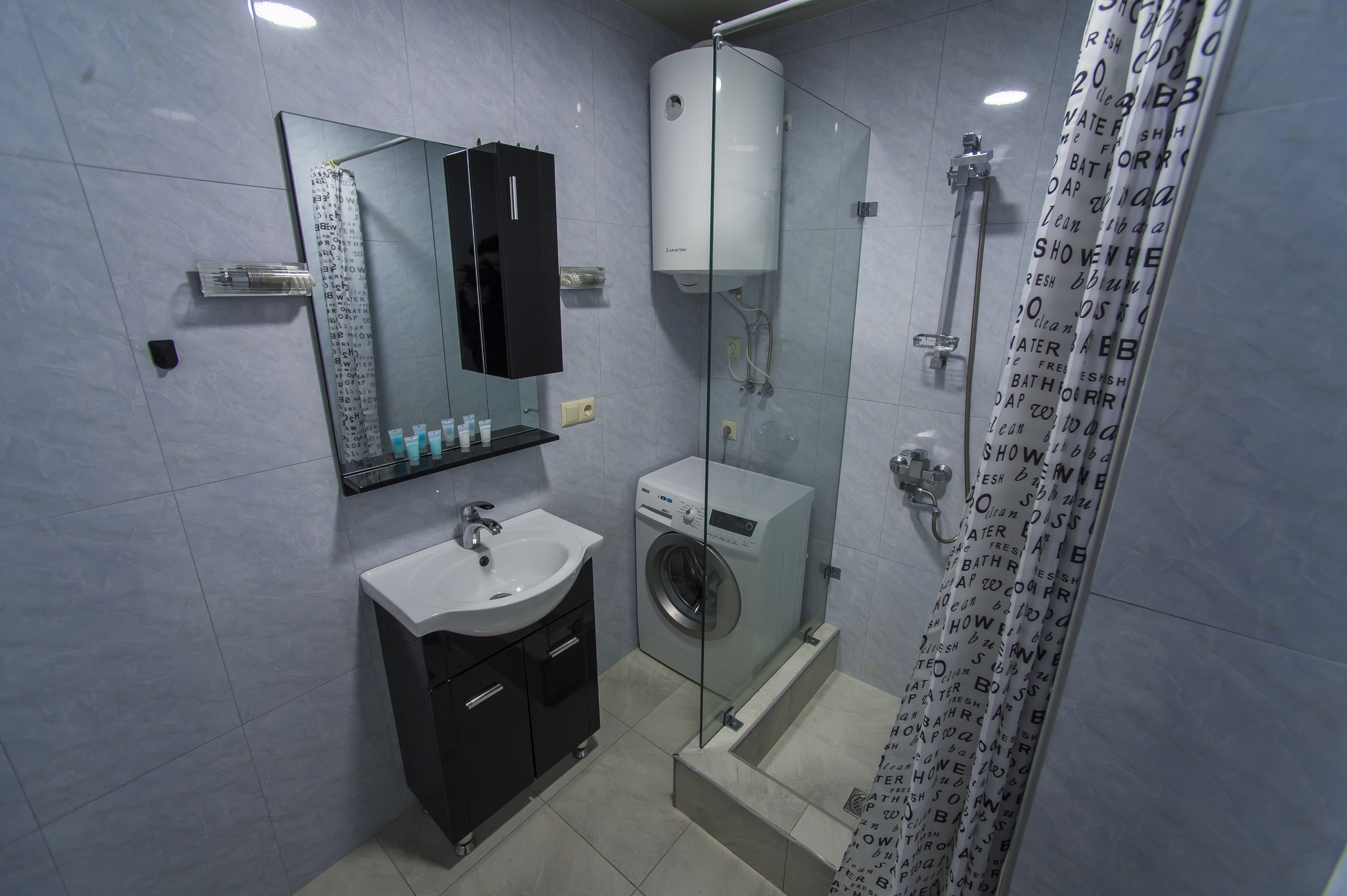 Une salle de bain moderne dotée d’une douche à parois de verre, d’un lave-linge encastré et d’un meuble-lavabo avec un miroir et des étagères.