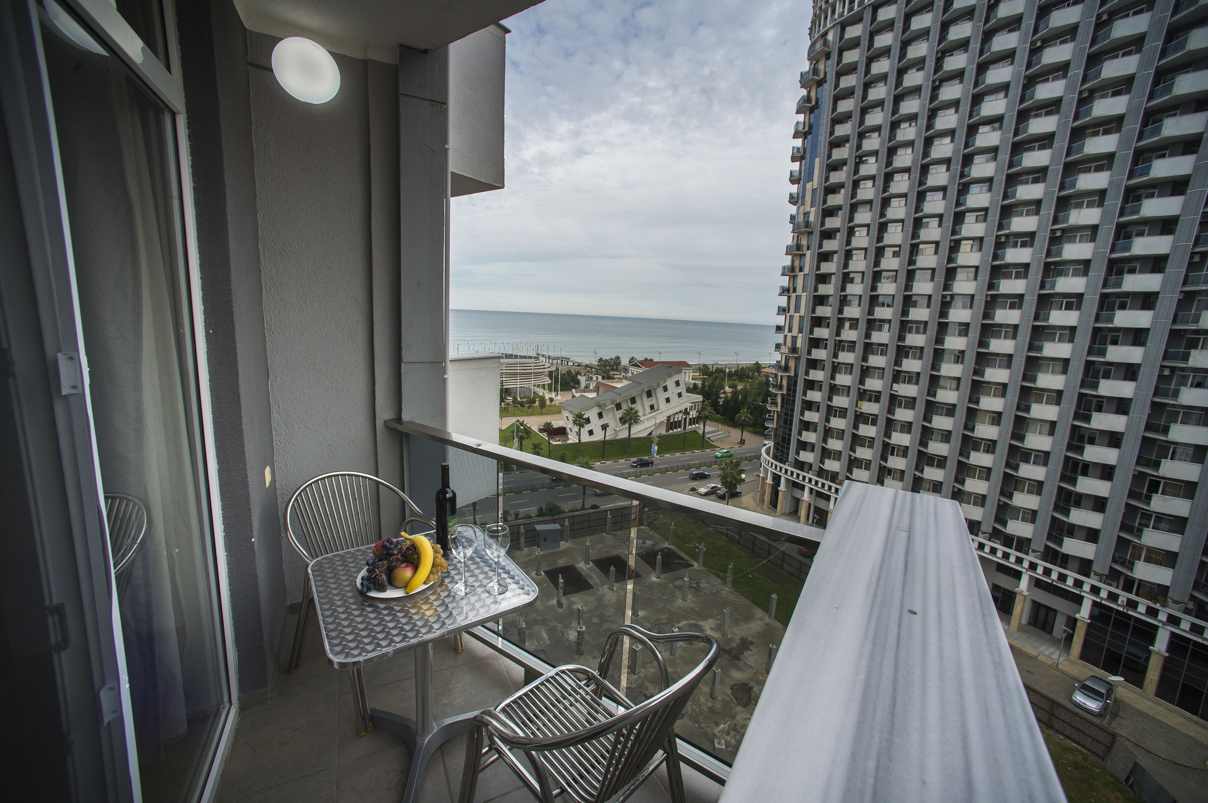 A balcony with a table, chairs, and a view of the sea and buildings.