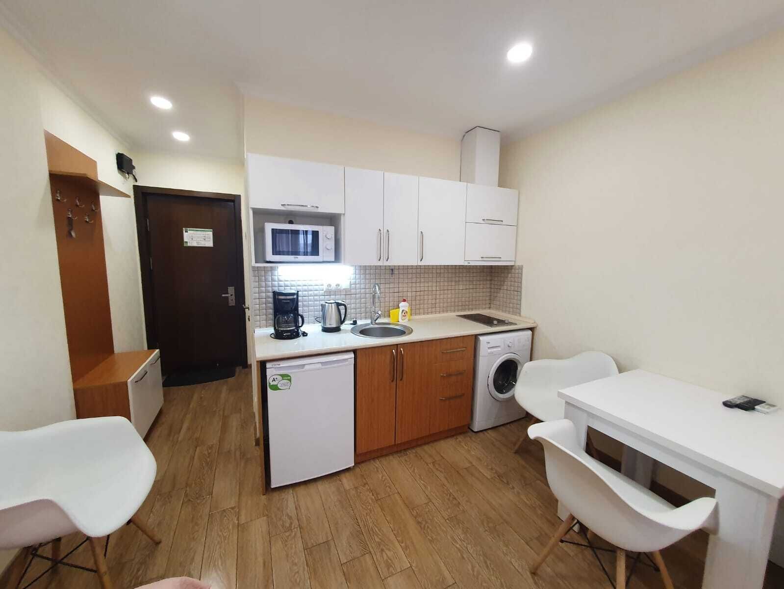 A compact kitchen with a microwave, coffee maker, sink, and washing machine.
