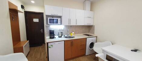 A compact kitchen with a microwave, coffee maker, sink, and washing machine.