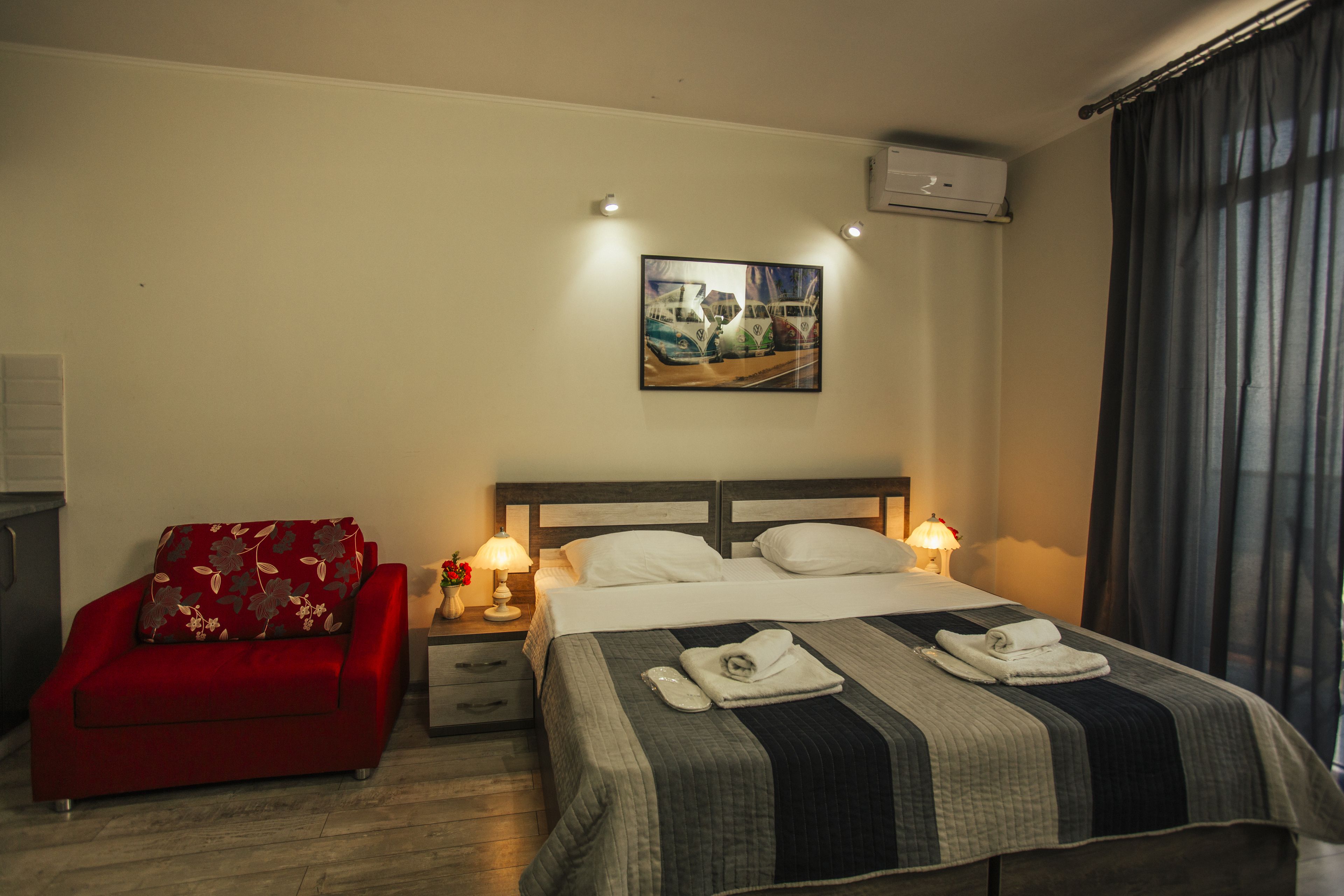 A hotel room with a bed, a red sofa, a painting on the wall, and two bedside lamps.