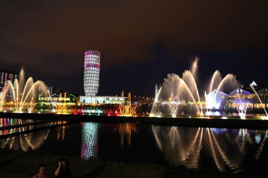 A nighttime view of a cityscape with illuminated buildings and a water fountain display.