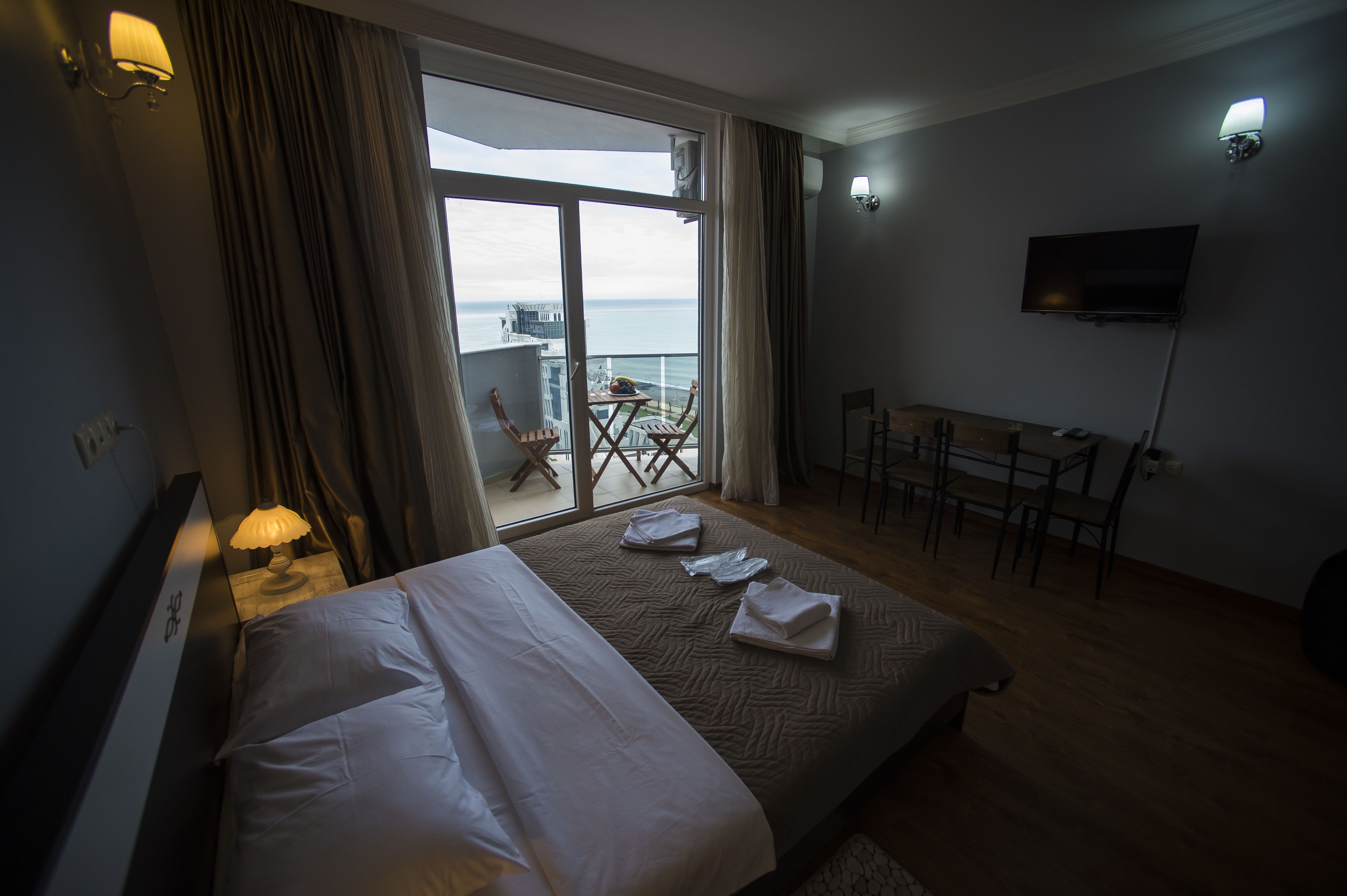 Ein Hotelzimmer mit Bett, Schreibtisch, Stuhl und einem Balkon mit Tisch und Stühlen.
