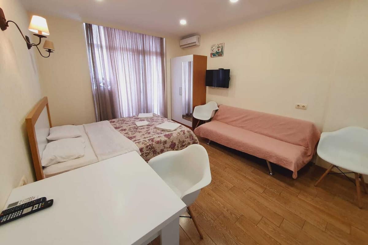 Ein Hotelzimmer mit Bett, Schreibtisch, Sessel, Sofa, Fernseher und Klimaanlage.