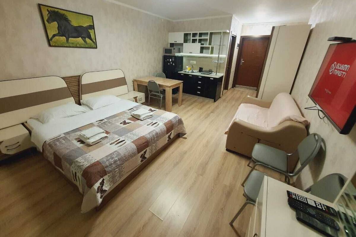 Ein Hotelzimmer mit Bett, Schreibtisch, Stuhl, einer kleinen Küchenzeile und einem Fernseher.