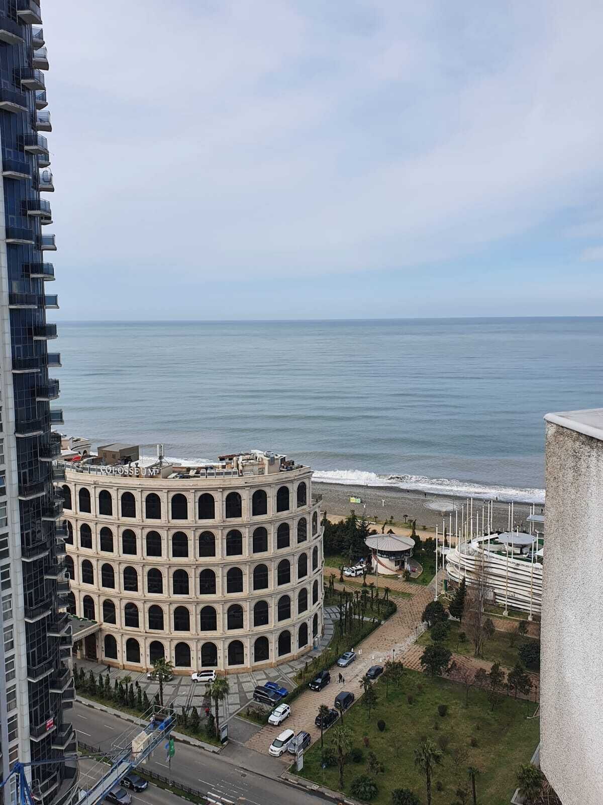 A multi-story building with a circular structure, a parking area, and a view of the ocean.