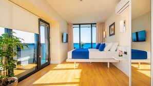 Une chambre d’hôtel moderne équipée d’un lit, d’une télévision, d’un balcon agrémenté d’une plante et offrant une vue sur la mer.
