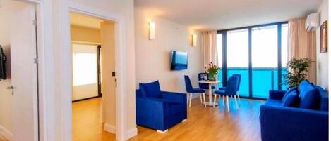 A modern living room with a sofa set, a dining area with chairs and a table, and a TV mounted on the wall.