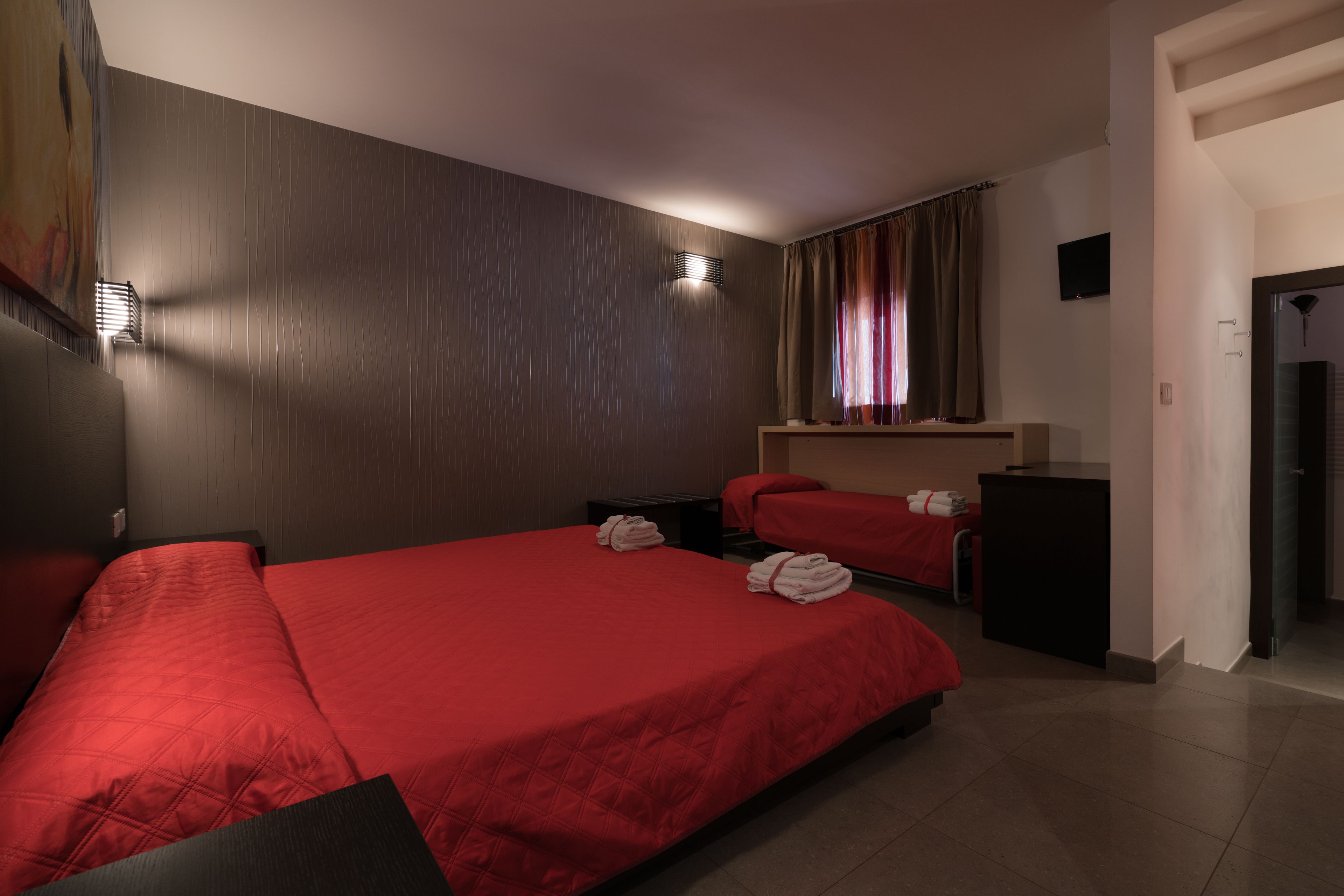 Habitación de hotel con dos camas, un escritorio, un televisor y una ventana con cortinas.