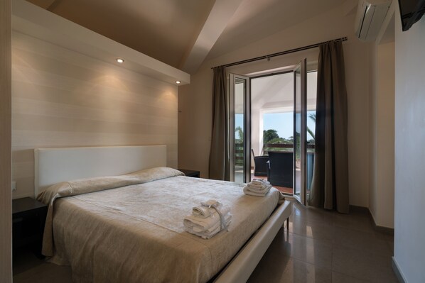 A modern hotel room with a large bed, a nightstand, a chair, and a view of the outdoors through a sliding glass door. - Bed and breakfast Nacorè (Massafra)