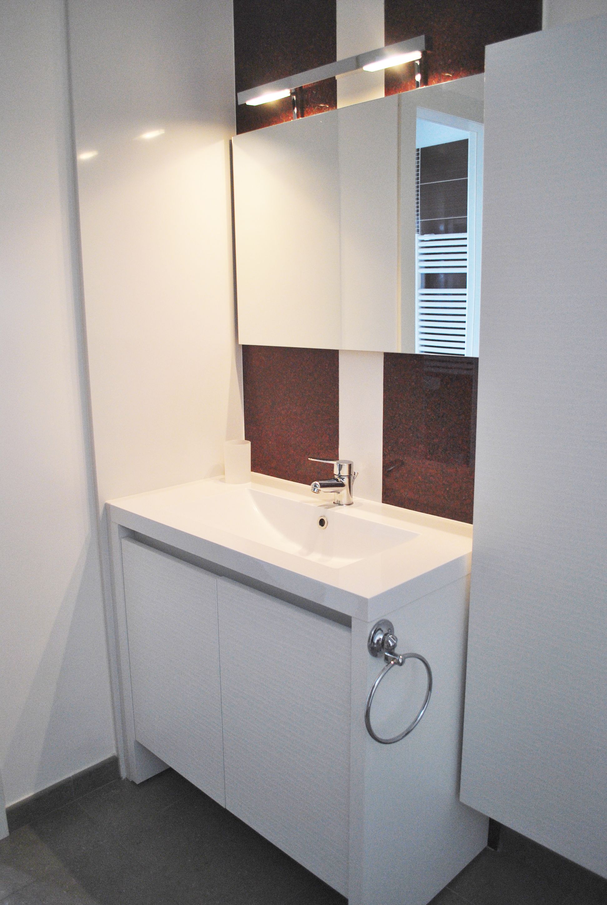 A modern bathroom with a white vanity, a mirror, and a towel ring.