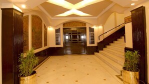 A grand lobby with a central staircase, a reception desk, and two potted plants. - Hotel Chanakya (Patna)