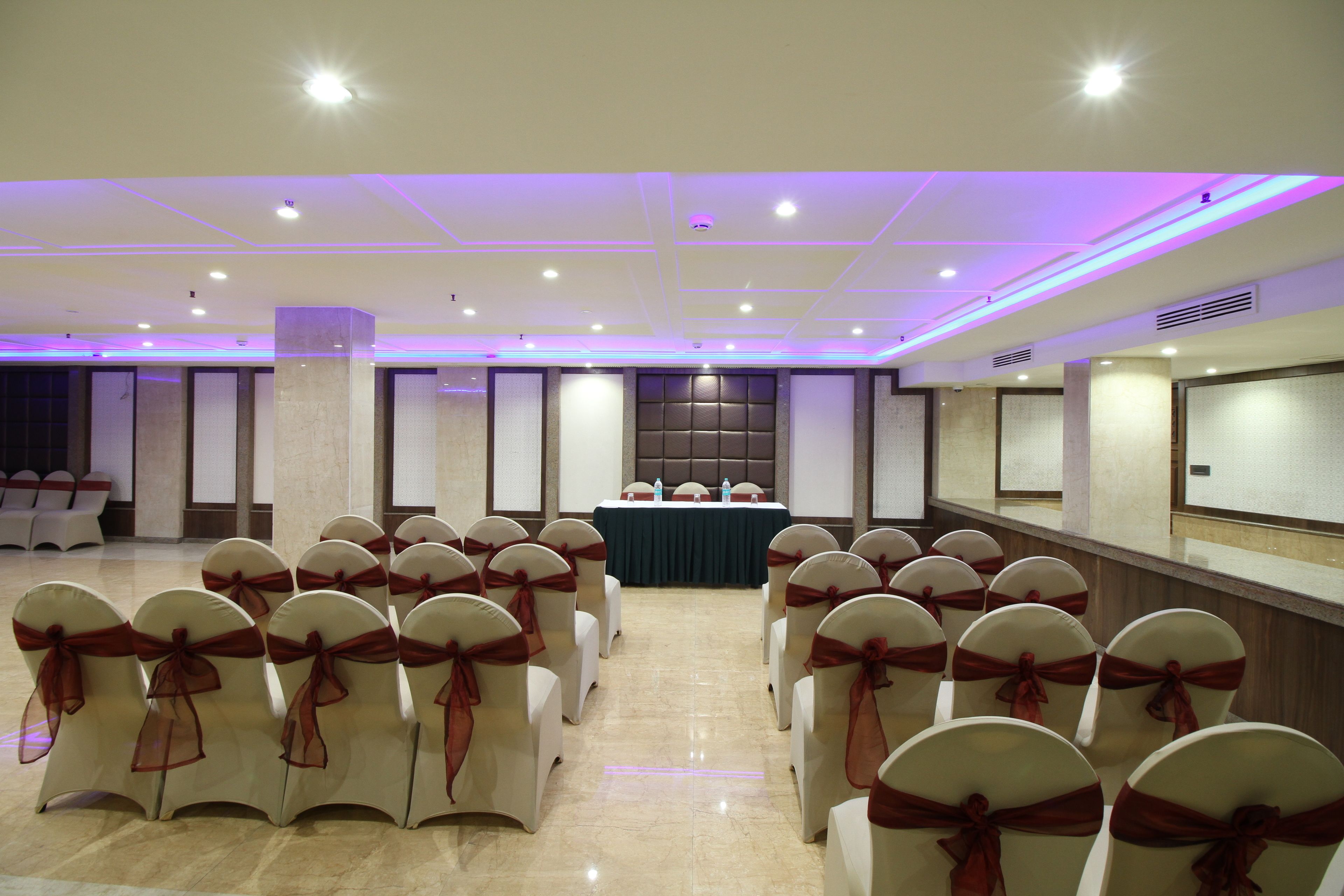 Un salón de conferencias con filas de sillas, una mesa y una pantalla al frente.