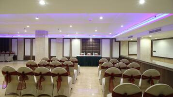 Un salón de conferencias con filas de sillas, una mesa y una pantalla al frente.