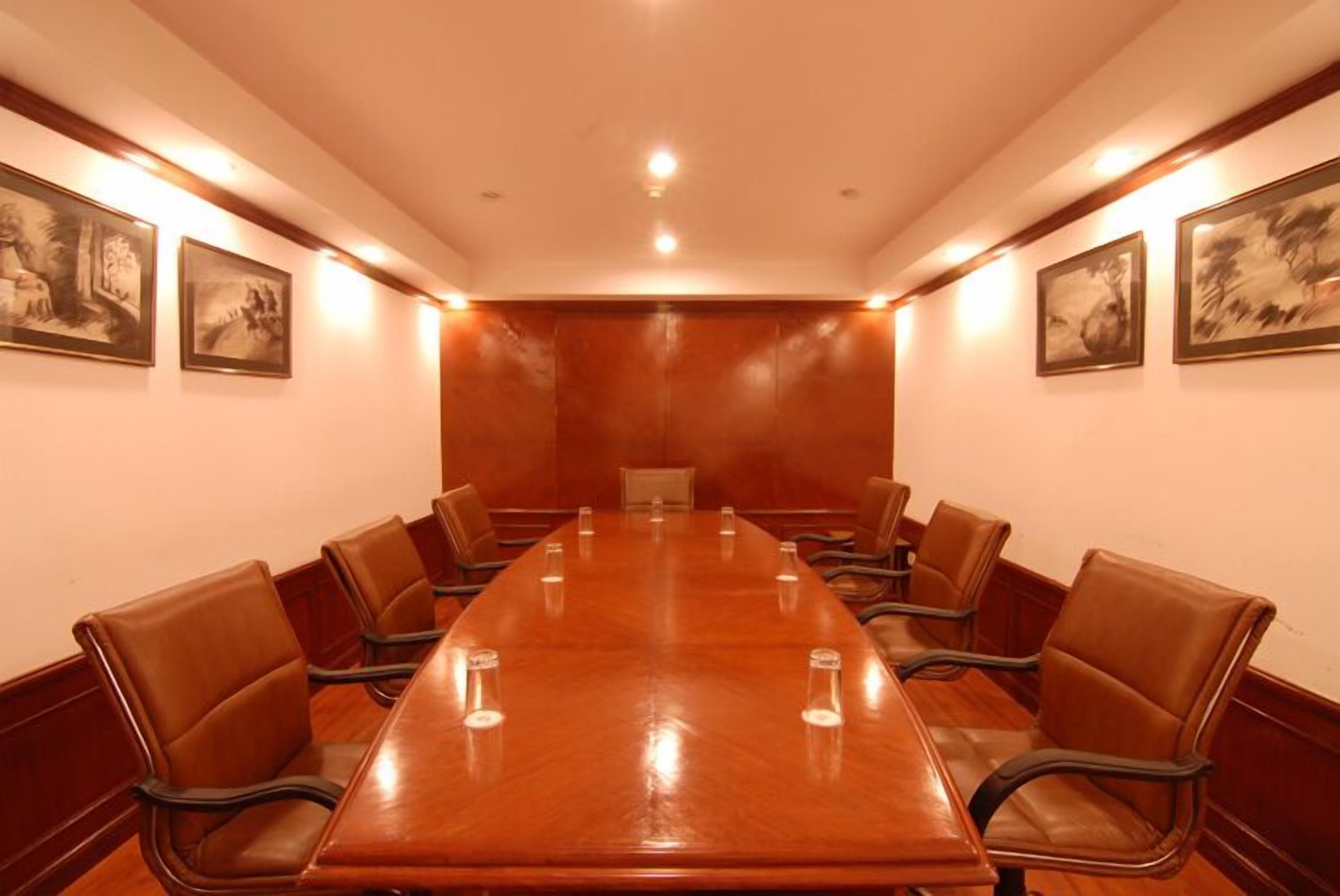 Un salón de conferencias con una larga mesa y sillas de cuero, cuadros en las paredes e iluminación empotrada.