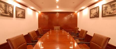 Un salón de conferencias con una larga mesa y sillas de cuero, cuadros en las paredes e iluminación empotrada.