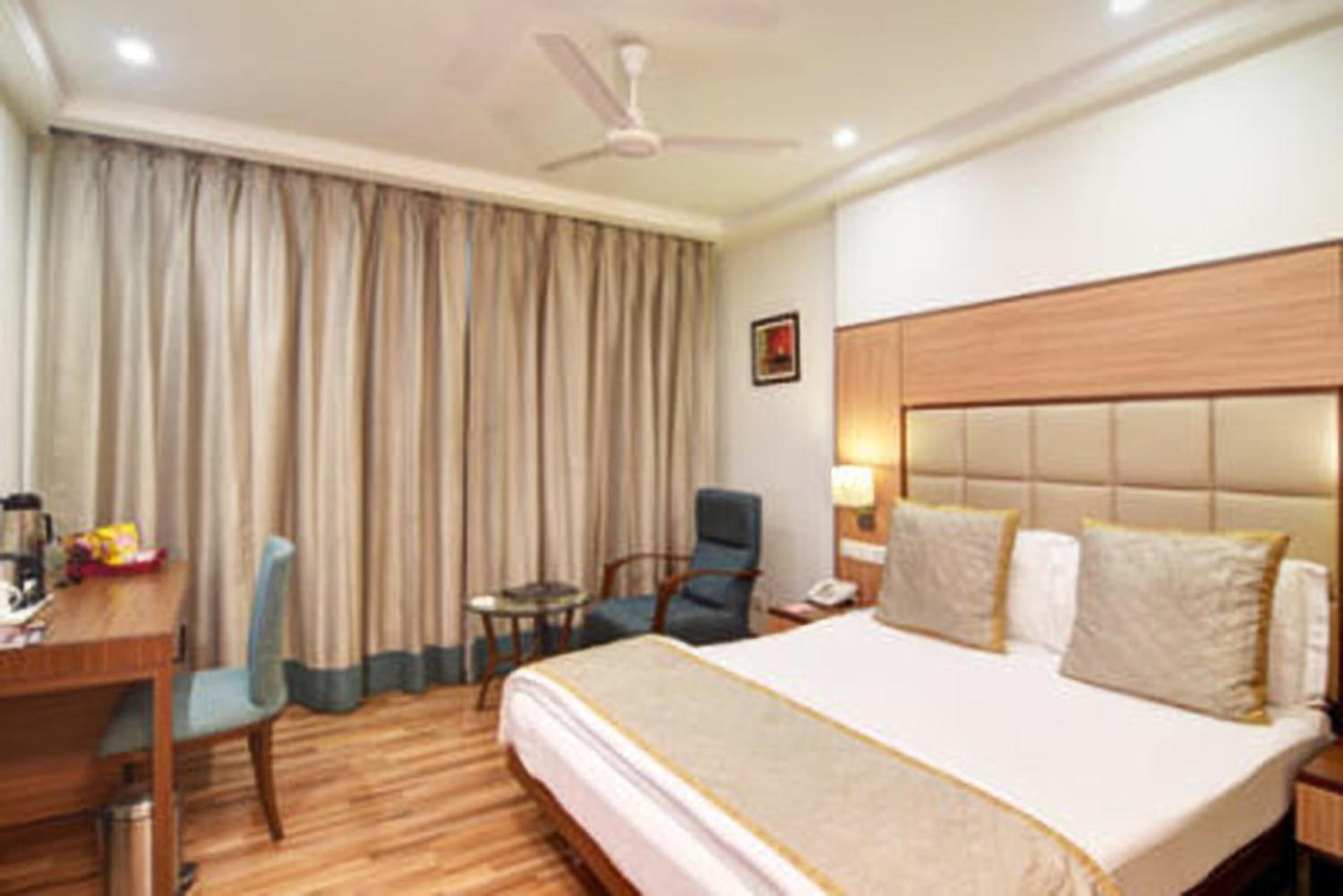 Habitación de hotel con cama, escritorio, silla, una mesita pequeña y un ventilador de techo.