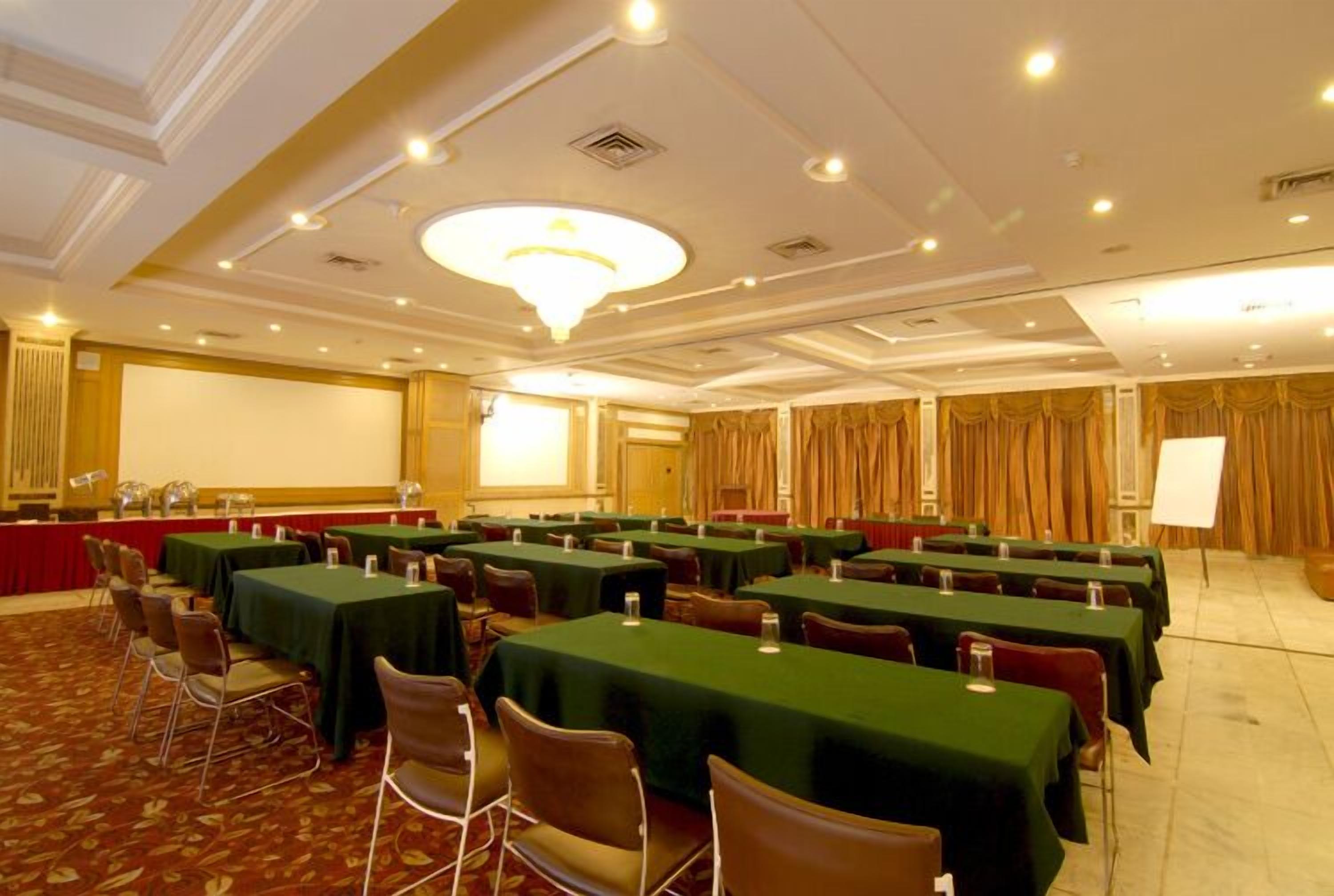 A conference room with multiple tables and chairs, a large screen, and a podium.