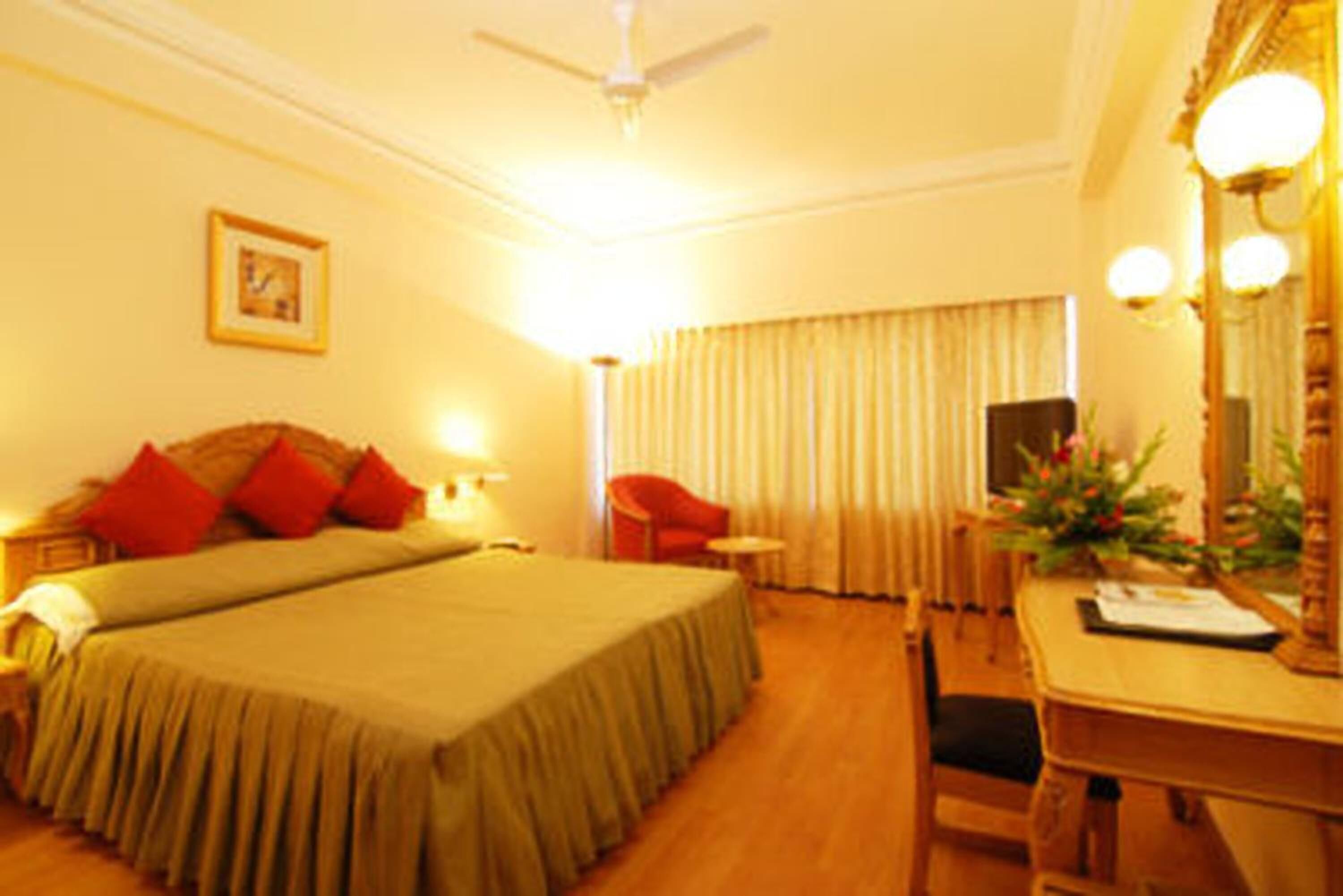 A hotel room with a bed, a desk, a chair, a ceiling fan, and a window with curtains.