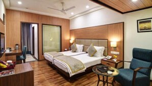A hotel room with two beds, a desk, a chair, and a small table. - Hotel Chanakya (Patna)