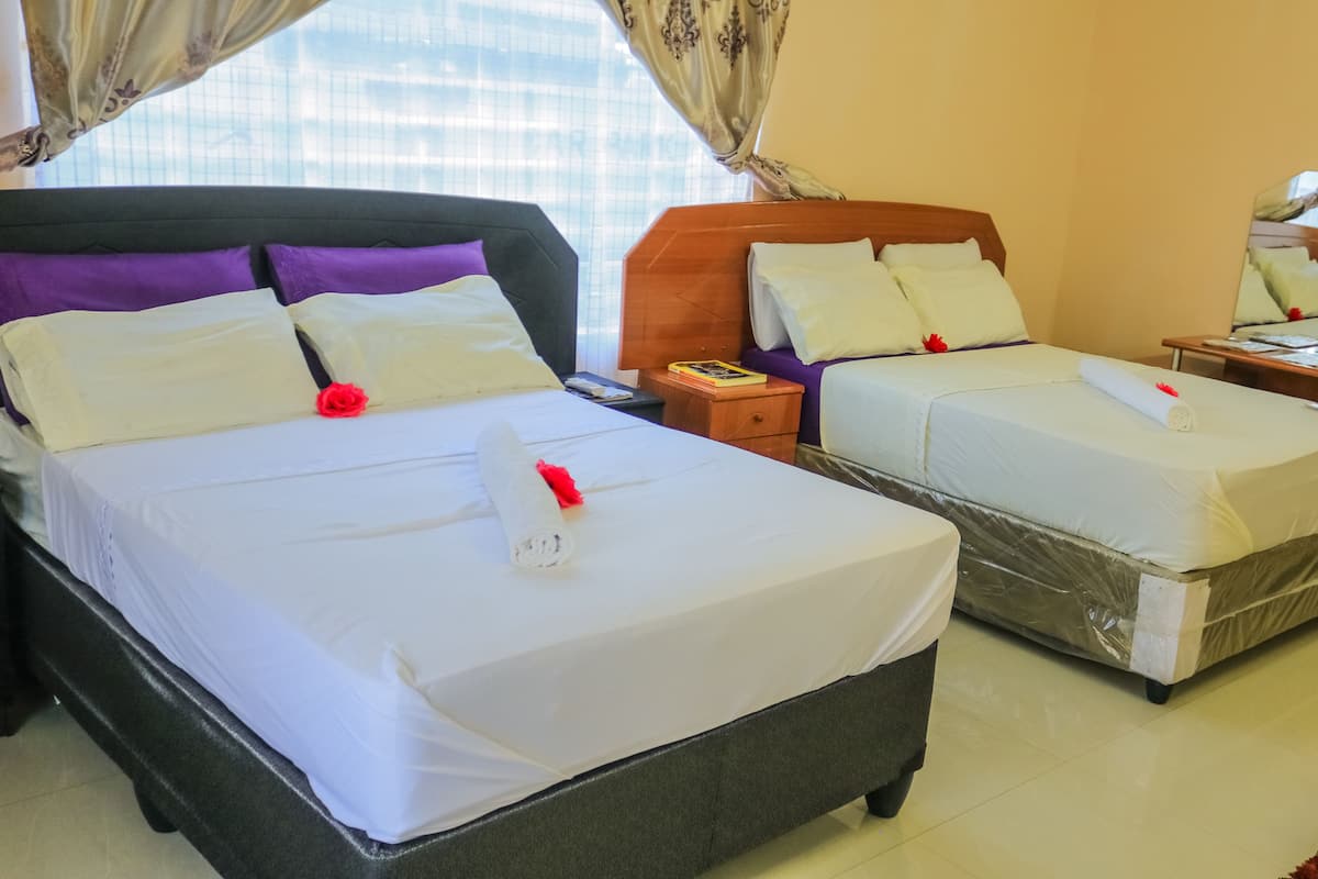 A hotel room with two beds, a wooden headboard, a nightstand, a mirror, and a window with curtains.