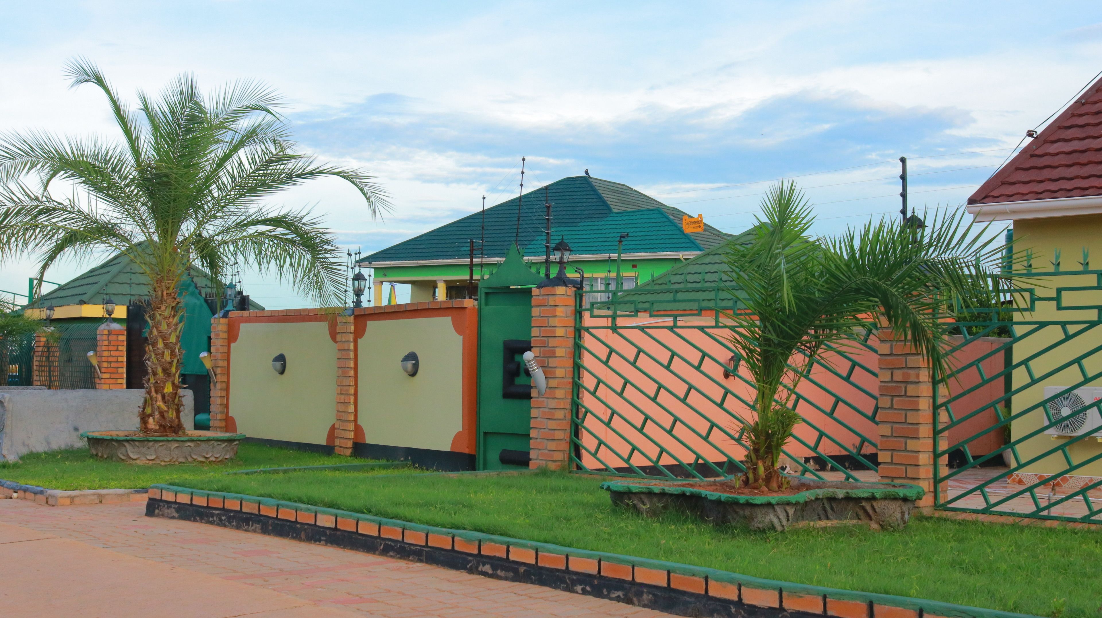 Un barrio residencial con una casa de techo verde, un muro de ladrillo y un acceso con portón.