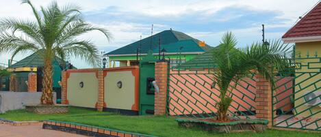Un barrio residencial con una casa de techo verde, un muro de ladrillo y un acceso con portón.
