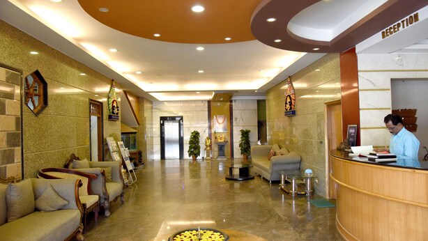 A hotel lobby with a reception desk, sofas, a coffee table with a bowl of fruit, and a reception area. - Sharada International Hotel (Udupi)