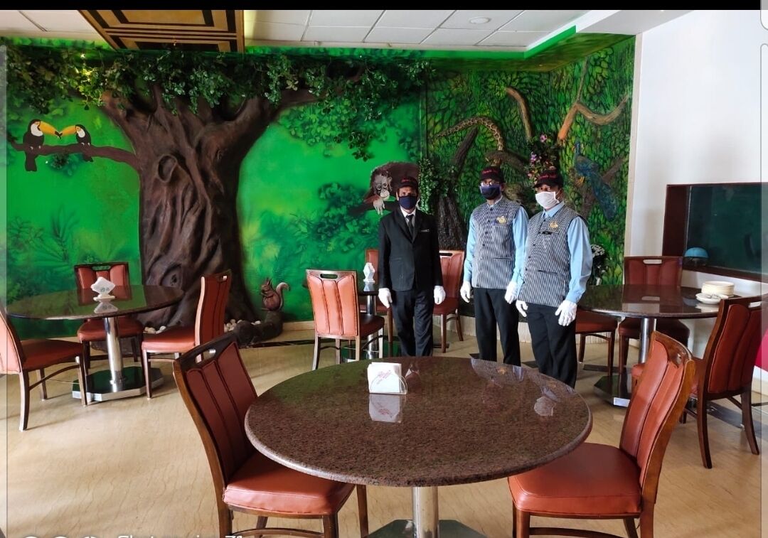 A room with a green mural of a tree and birds, a round table with chairs, and a television on the right.