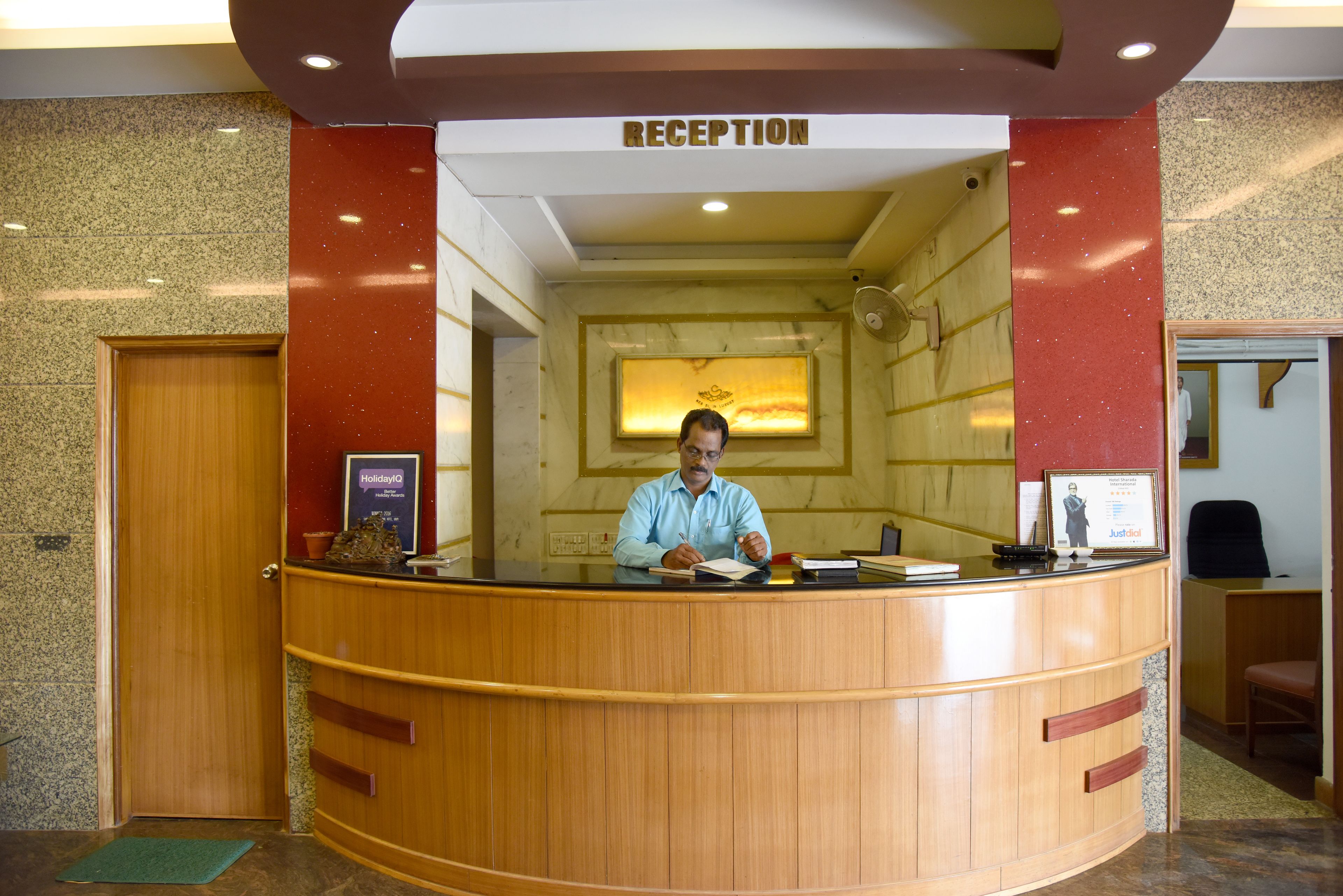 A reception desk with a wooden finish, a sign above it reading "RECEPTION", and a framed picture on the wall behind the desk.