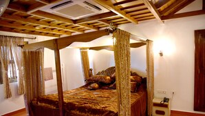 A four-poster bed with a canopy, a bedside table with a telephone, and a wall-mounted light fixture. - Sharada International Hotel (Udupi)