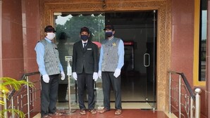 Three individuals standing in front of a building entrance with a glass door and a decorative frame. - Sharada International Hotel (Udupi)