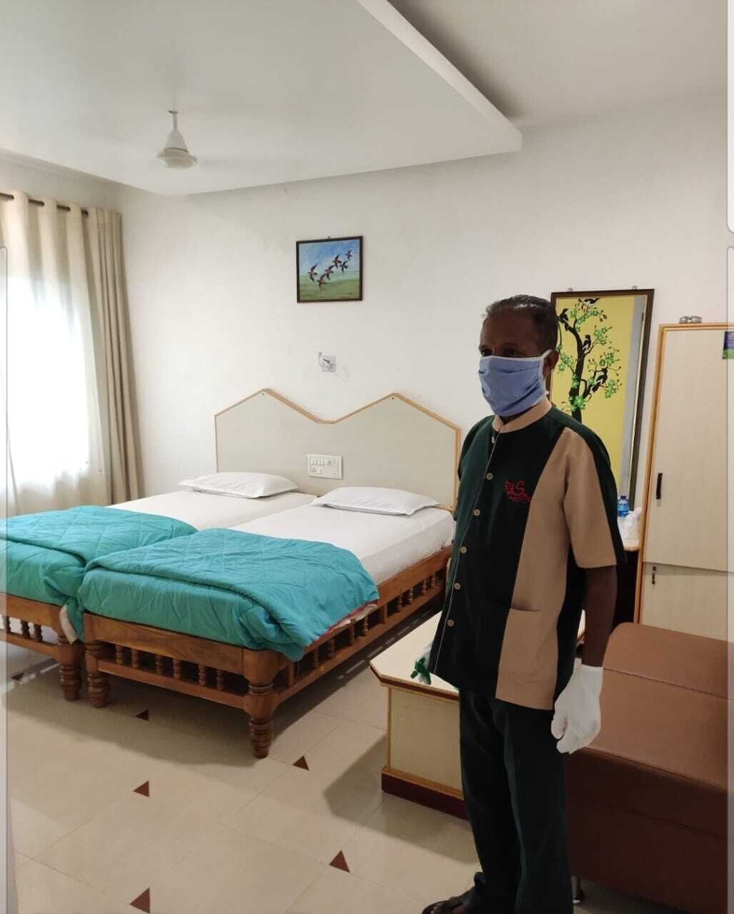 A hotel room with a bed, a desk, a chair, a wardrobe, and a painting on the wall.