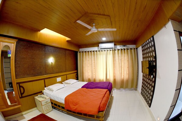 A room with a bed, a ceiling fan, an air conditioning unit, and a curtain. - Sharada International Hotel (Udupi)