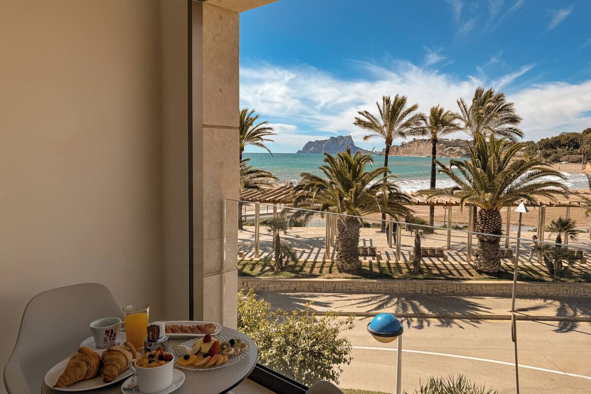 Un balcon avec des éléments pour le petit-déjeuner, une vue sur la plage, des palmiers et une montagne en arrière-plan.