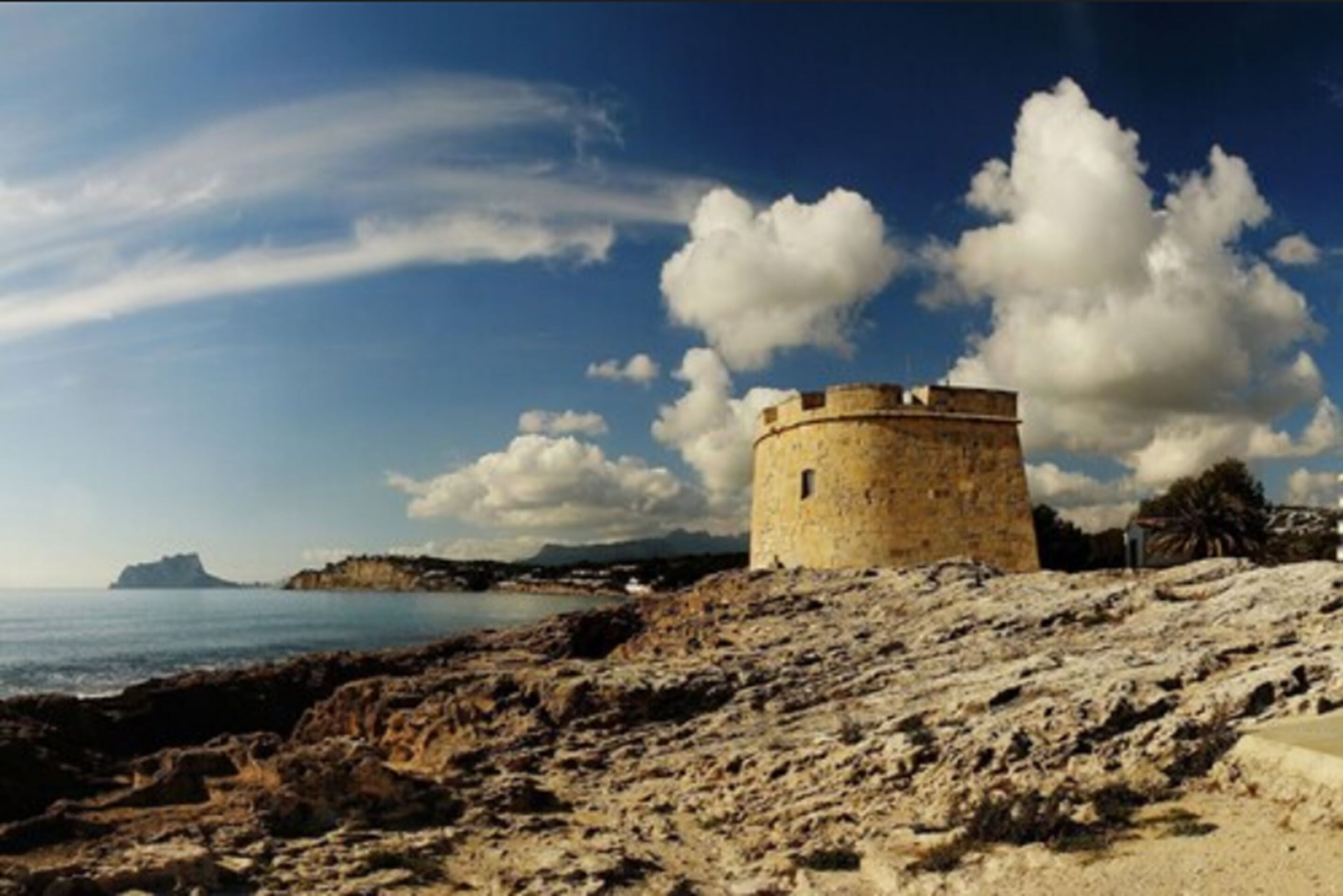 A coastal stone tower with a clear view of the sea and distant land.