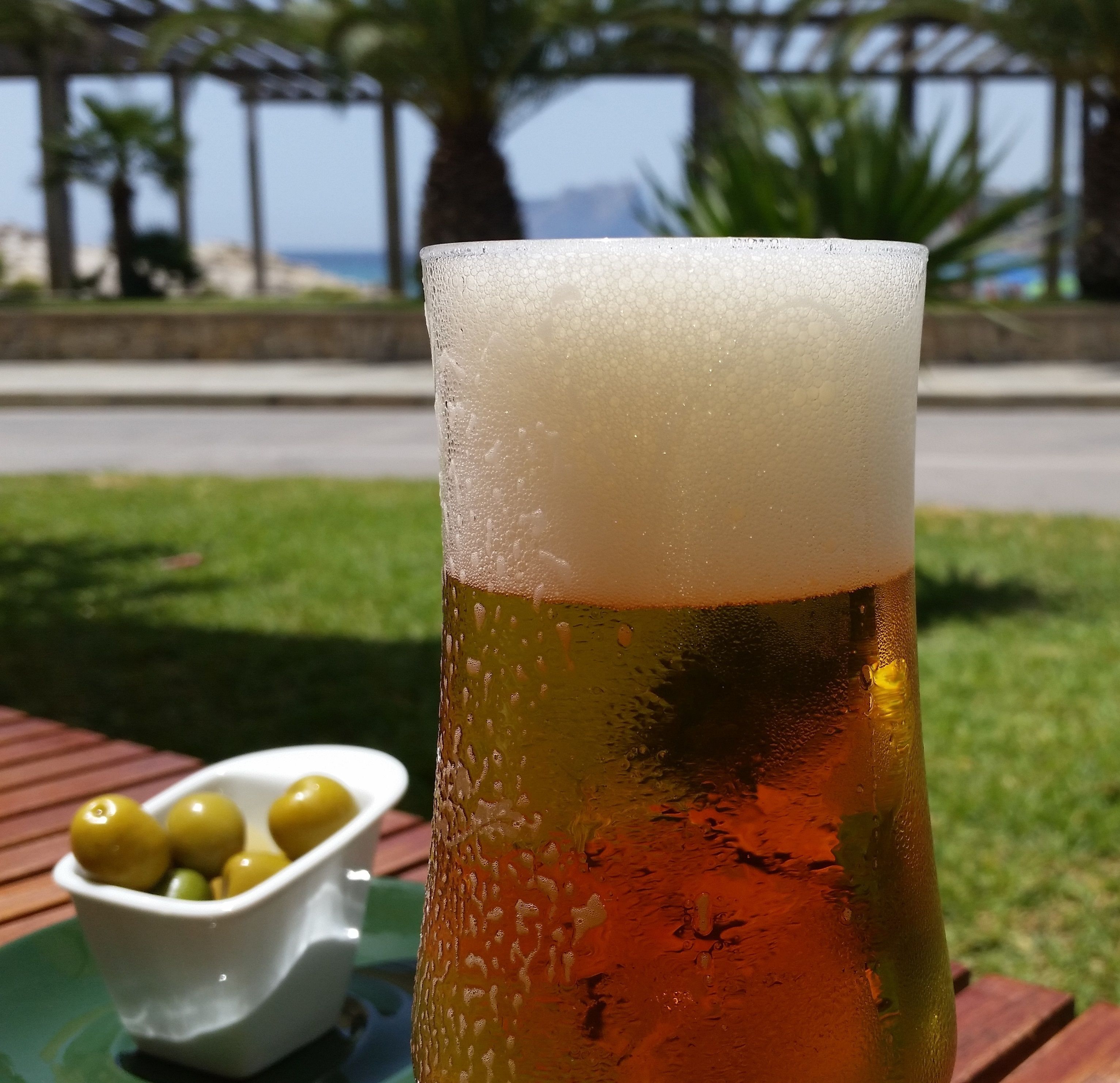 Un grand verre de bière, avec une mousse généreuse, posé sur une table en bois à l’extérieur.