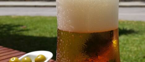 Un grand verre de bière, avec une mousse généreuse, posé sur une table en bois à l’extérieur.