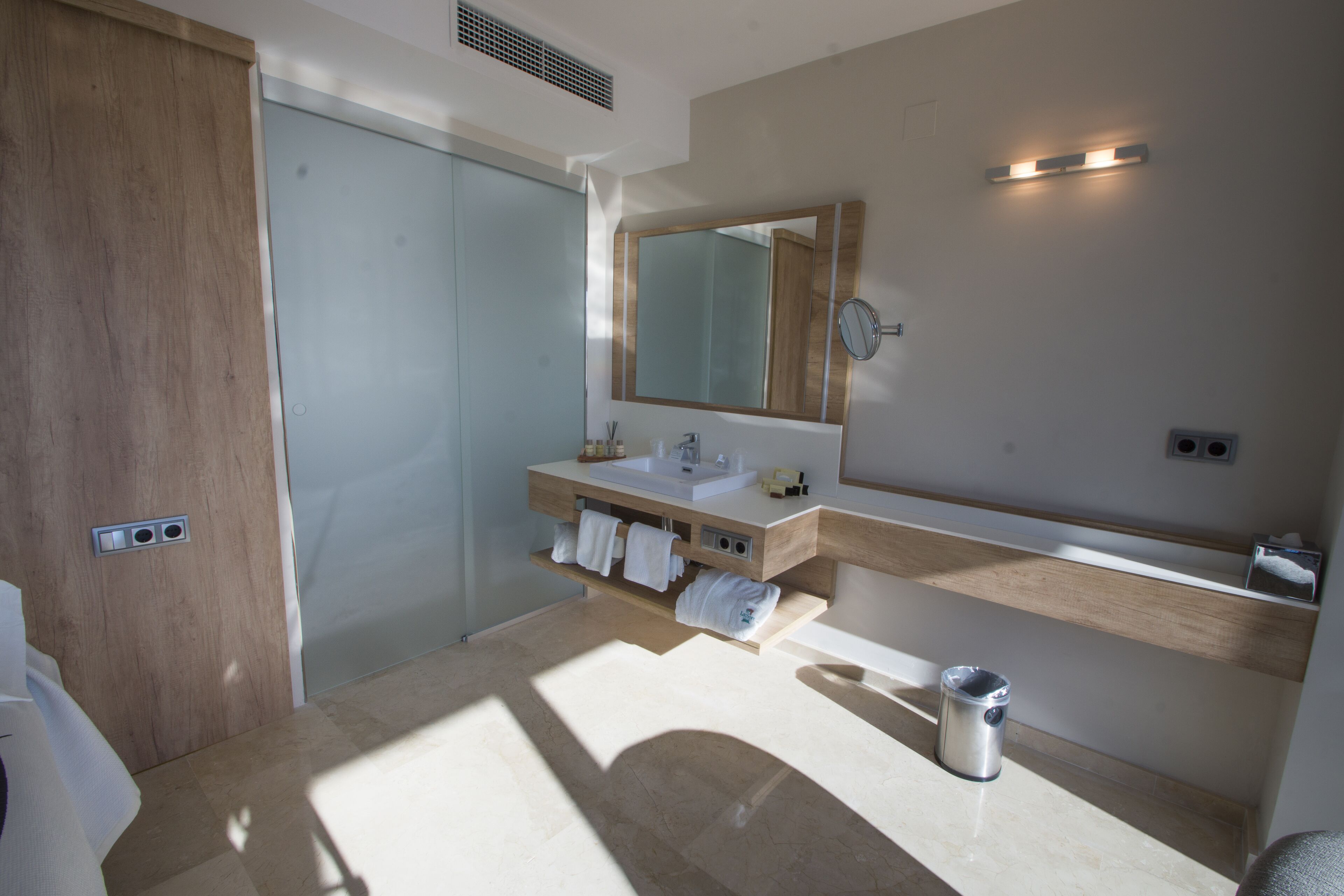 A modern bathroom with a wooden door, a large mirror, a sink, and a towel rack.