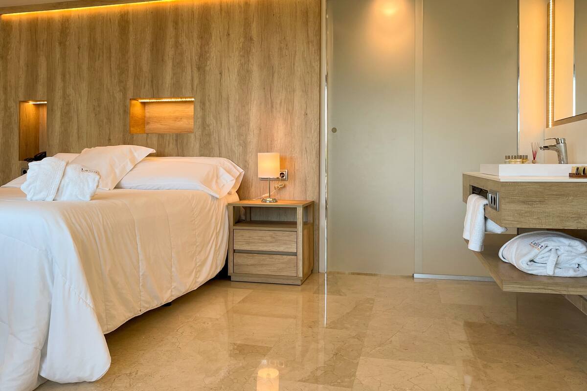 Une chambre d’hôtel comprenant un lit, une table de chevet, une lampe et une salle de bain avec un lavabo et un miroir.