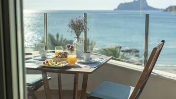 A balcony with a table set for breakfast, overlooking the sea.