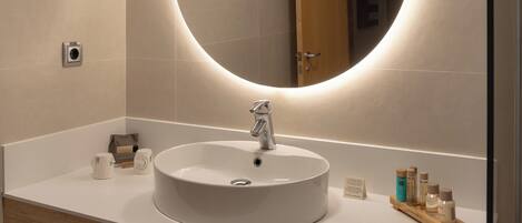 A modern bathroom with a round sink, a mirror with a circular light, and toiletries on the counter.