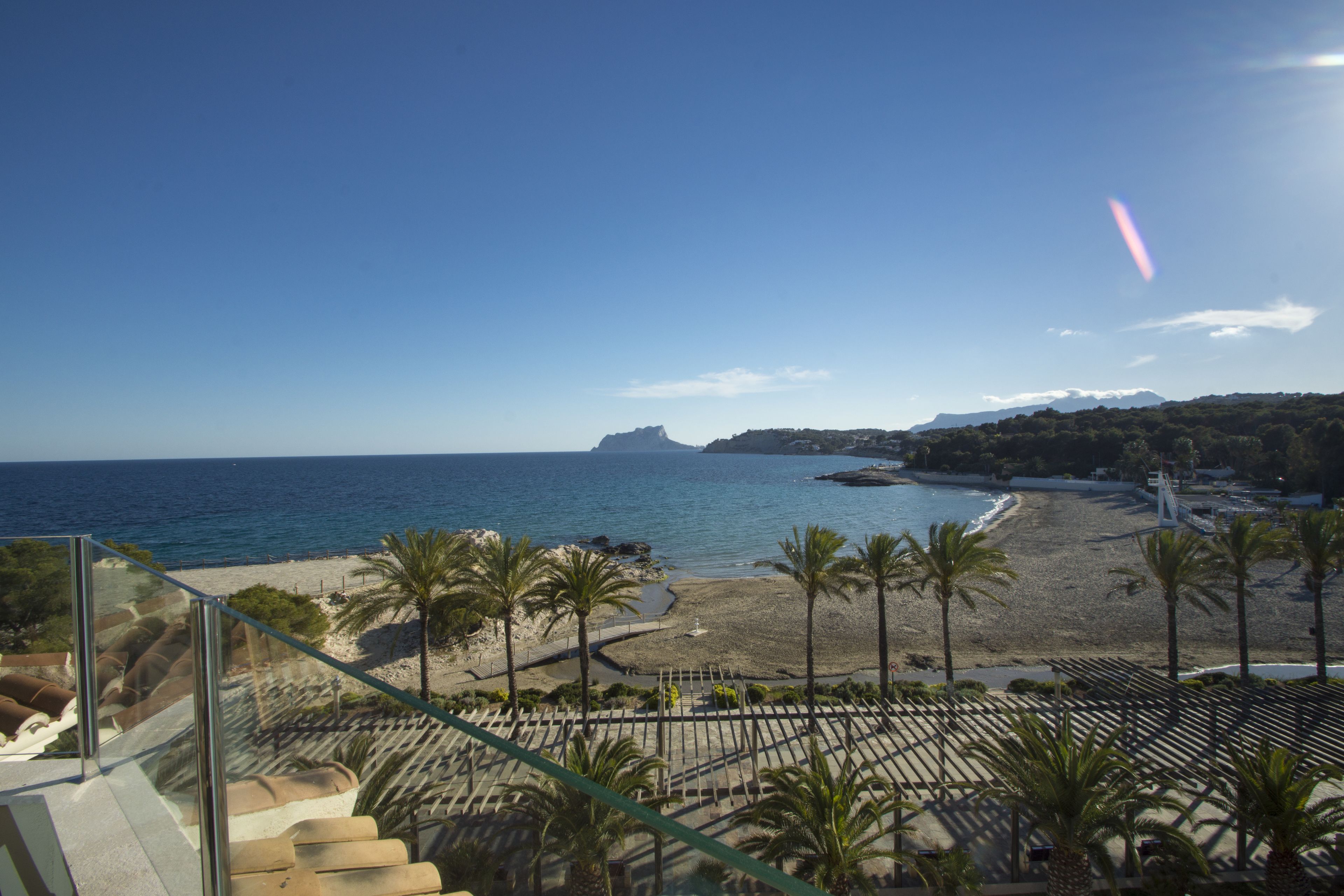 Vista a la playa desde un balcón con palmeras y cielo despejado.