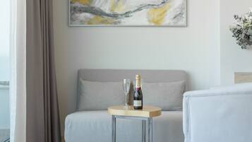 Une pièce moderne avec un canapé gris, une petite table ronde sur laquelle se trouvent une bouteille de champagne et un verre, et un grand tableau abstrait accroché au mur.