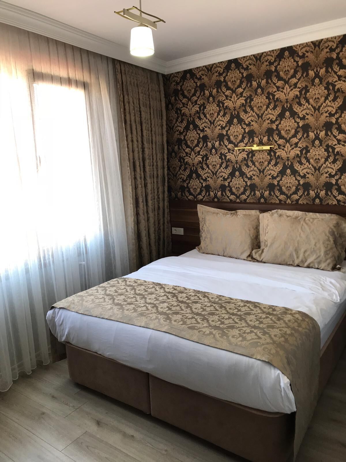 Una habitación de hotel con una cama grande, cabecera con un diseño decorativo y una ventana con cortinas.