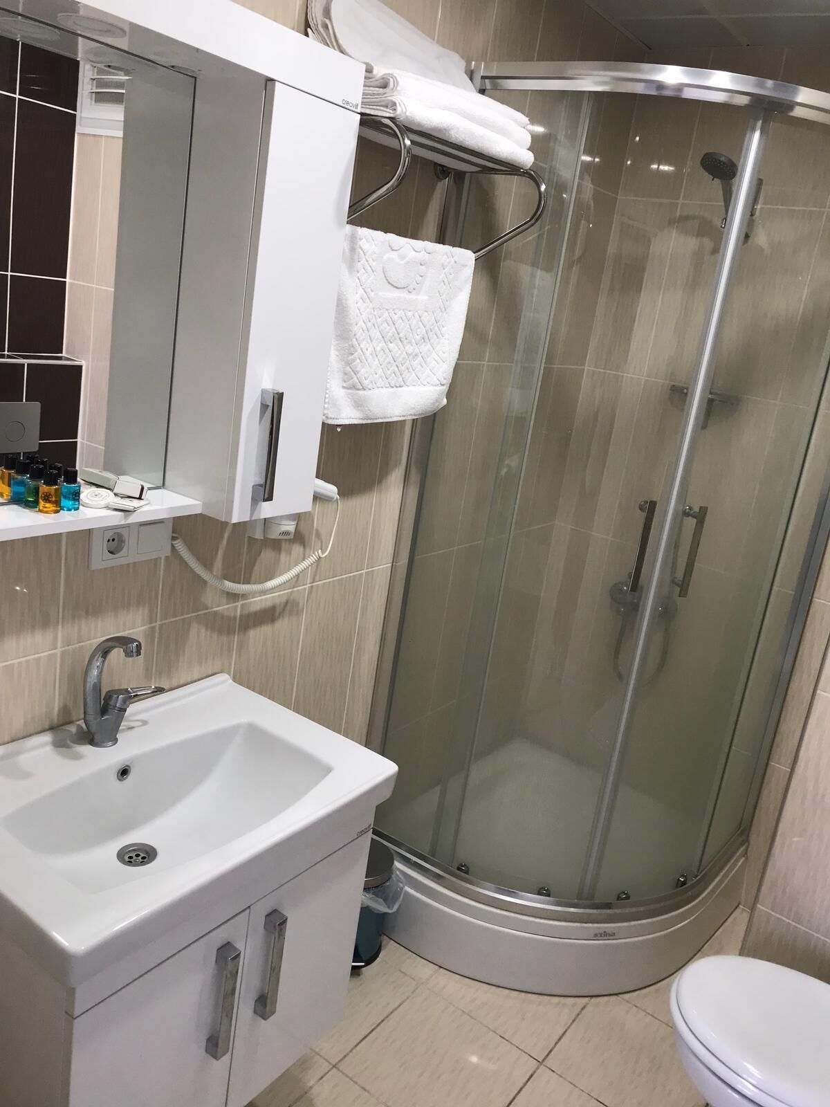 Un baño moderno con cabina de ducha de vidrio, un lavabo blanco con espejo arriba y un inodoro.