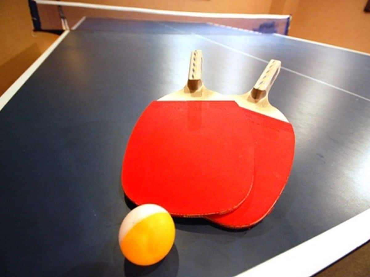 A ping pong table with two red paddles and a yellow ball.