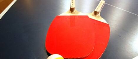 A ping pong table with two red paddles and a yellow ball.