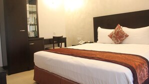 Hotellihuone, jossa on suuri sänky, puinen vaatekaappi, työpöytä ja peili.