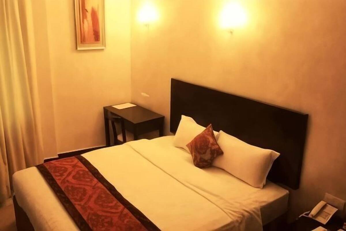 A hotel room with a bed, a nightstand, and a wall-mounted lamp.